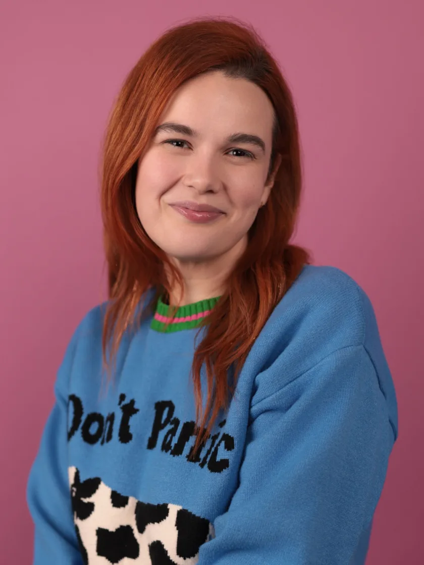 Stephanie Hind, in a blue “Don’t Panic” sweater against a pink backdrop